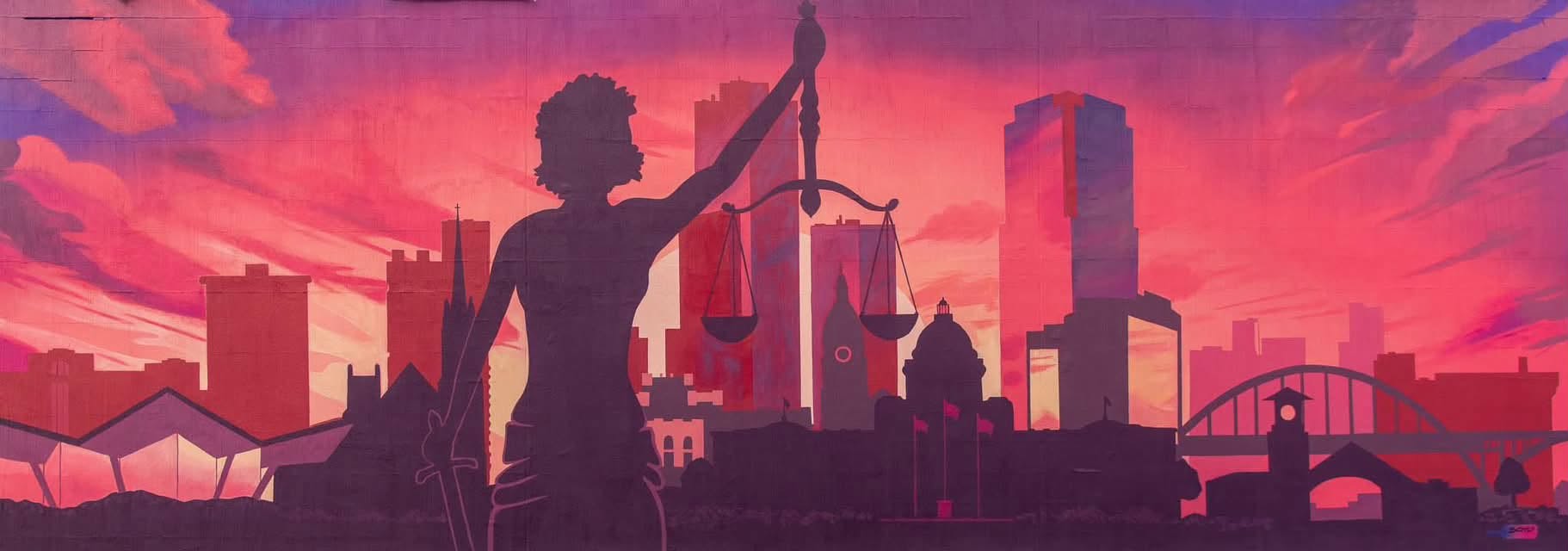 A mural of Lady Justice silhouetted against the Little Rock skyline at sunset