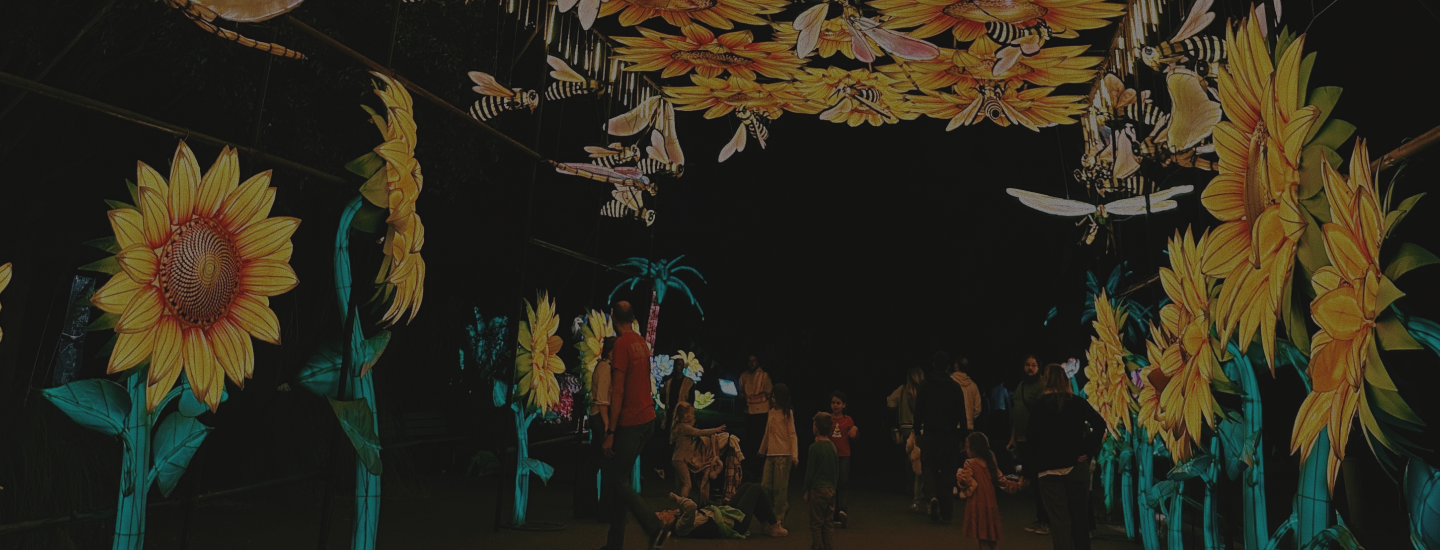 Visitors walking beneath illuminated sunflowers and bees