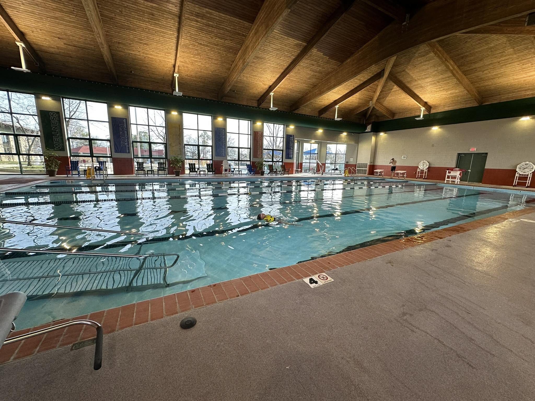 A swimmer doing laps in the indoor pool at Jim Dailey Fitness & Aquatic Center, beneath a wood-beamed ceiling and tall windows