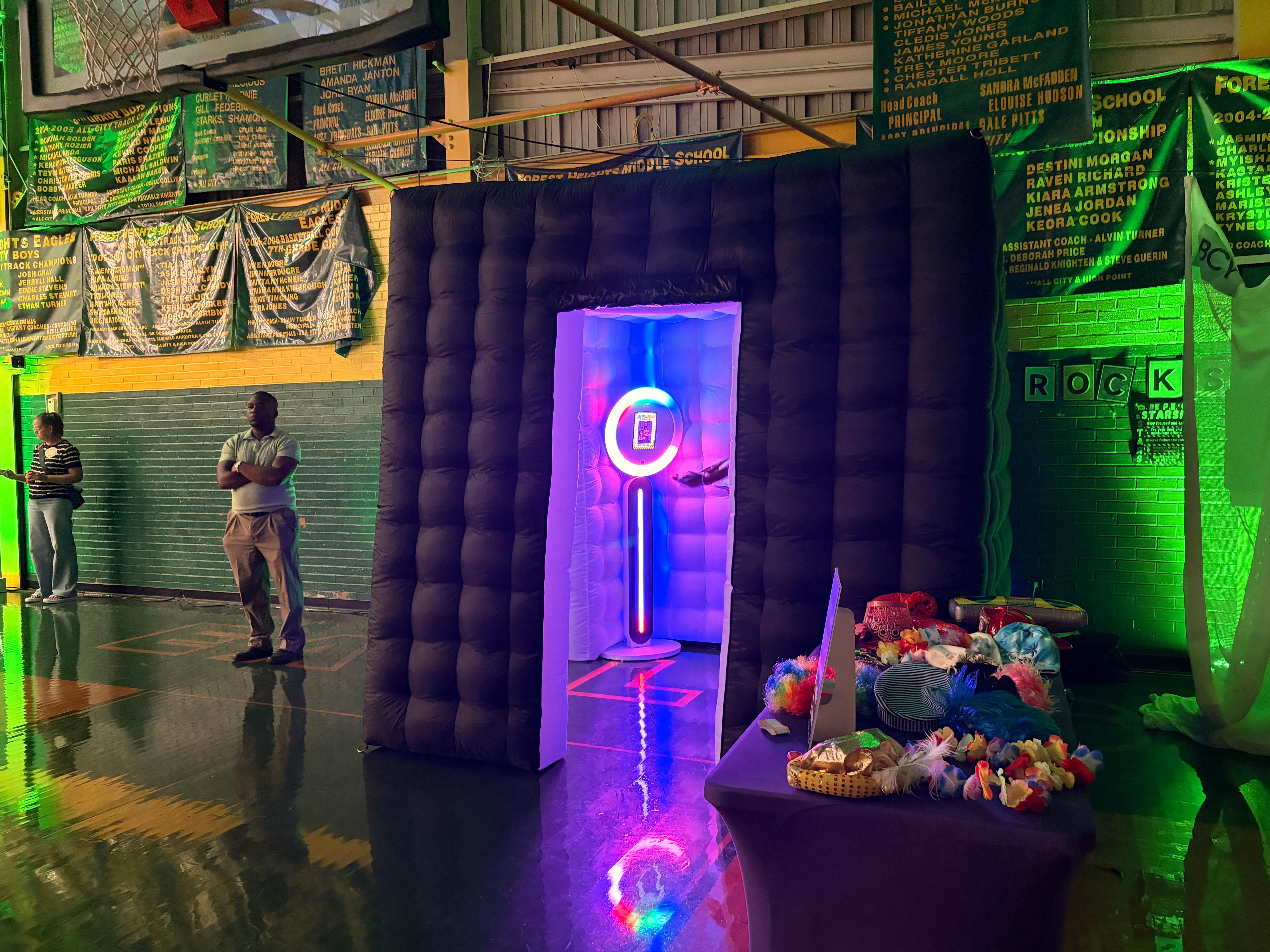 A glowing inflatable photo booth and a table of party props set up in a school gym for a Rocktown Realness event